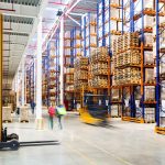 A large warehouse with many shelves of stock and forklifts driving around